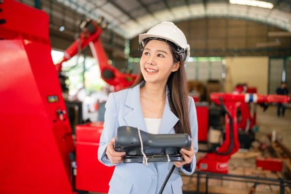 A woman holding a crane part in a garage