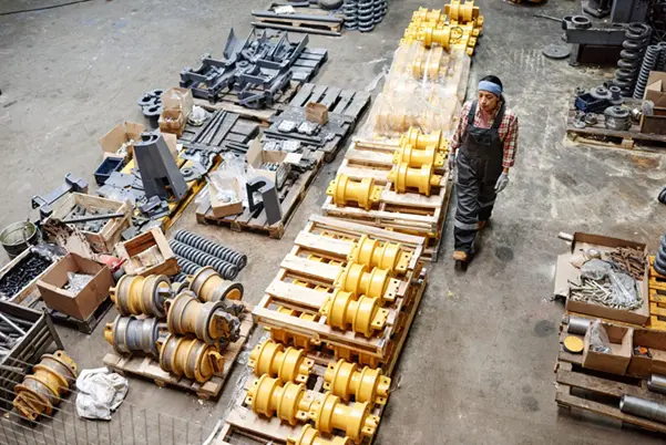 A mechanic inspecting rows of organized crane parts and machinery components on pallets