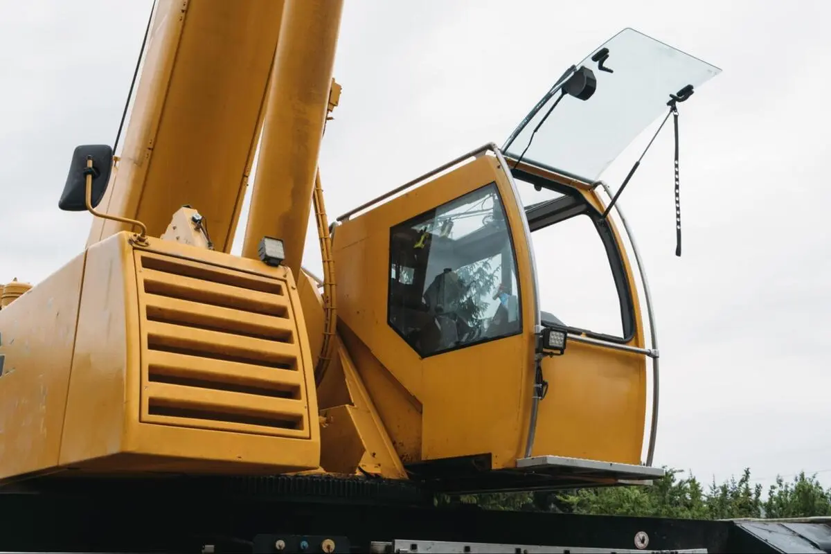 Crane Equipment Repair Planning Spare Parts Close-up low-angle view of a yellow heavy construction crane cab and boom against an overcast sky, illustrating crane equipment requiring planned part procurement
