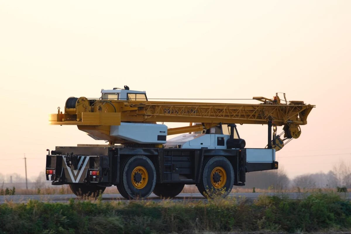 Mobile crane on the road Yellow mobile crane with extended boom traveling on a road at dusk