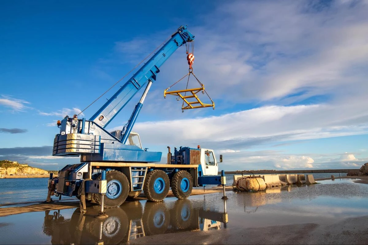 Rough-terrain crane lifting load Mobile rough-terrain crane lifting a yellow lifting frame near a waterfront site