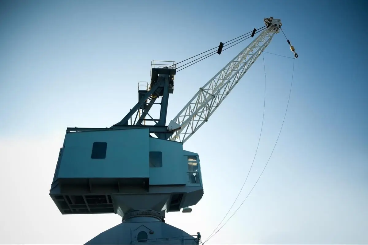 Teal Kobelco crawler crane boom against a clear blue sky